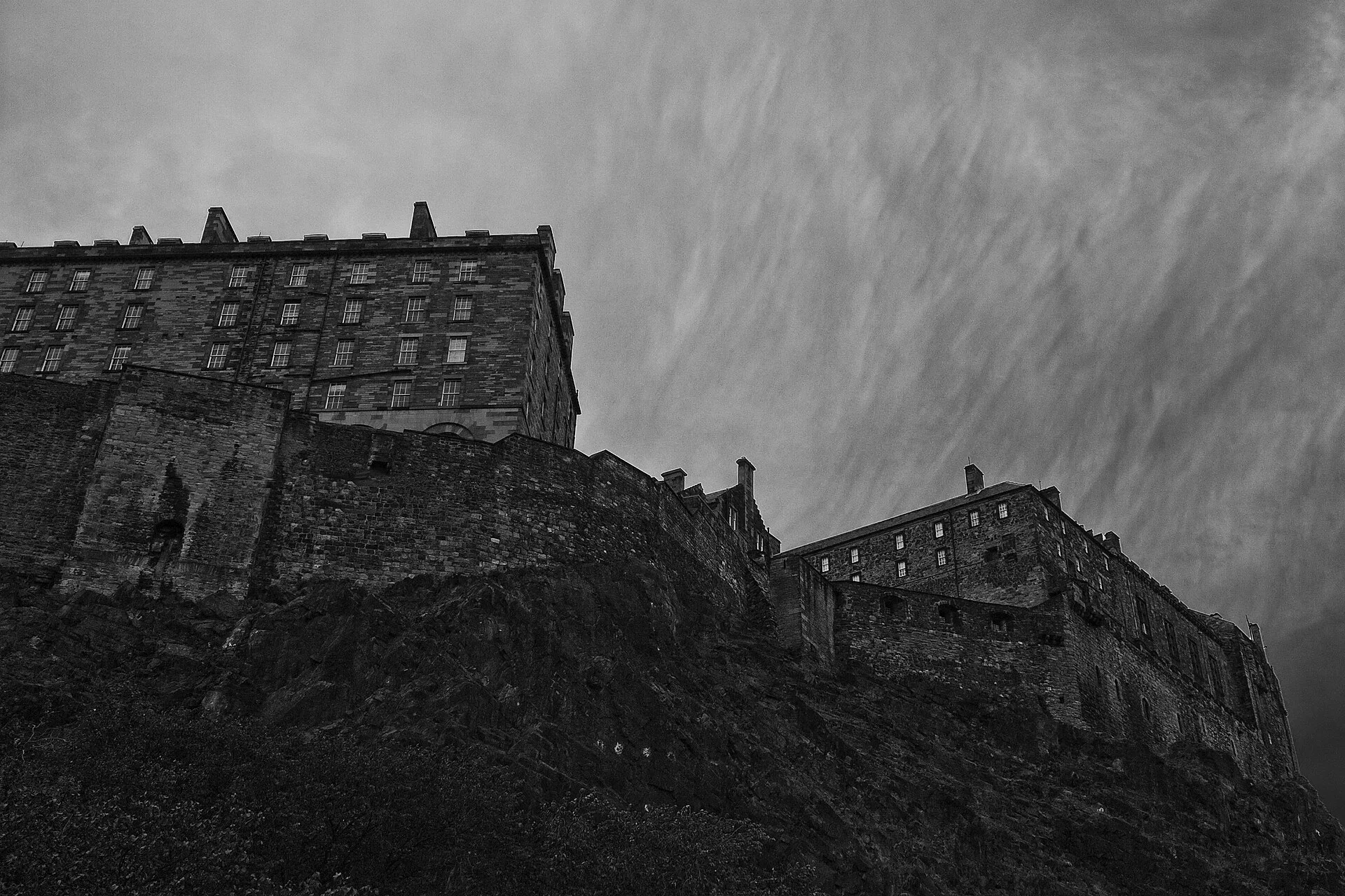 A monochrome photograph of Edinburgh Castle rising above the rock.